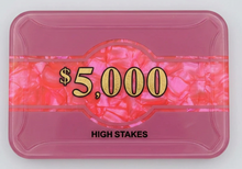 A pink high-stakes gaming chip tray or card with a marbled pink and orange center band featuring the text '$5,000' in gold, and 'HIGH STAKES' printed in black below, shown on a light gray background.
