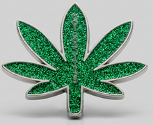 A green glitter cannabis leaf-shaped brooch with a silver metal border, centered on a light gray background.