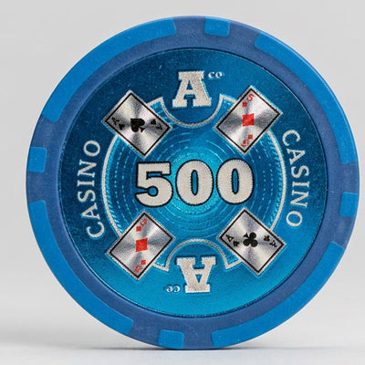 A single blue 500 casino chip with gold and white details stands upright on a tan tabletop in front of a black plastic tray, with other packaged items blurred in the foreground.