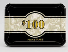 A black plastic high-stakes poker chip bin with a clear front label reading '$100 HIGH STAKES', shown on a tabletop with other bins and plastic bags in the background.