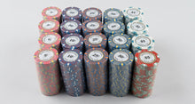 A set of stacked poker chips in multiple denominations, including $5, $10, $25, and $50, arranged on a light-colored wooden surface.