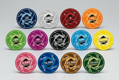 A set of circular gaming chips arranged in three rows on a light gray background. The chips come in multiple colors including blue, silver, red, orange, green, pink, black, light blue, yellow, brown, and dark green, each with different denominations from 25 to 100,000.